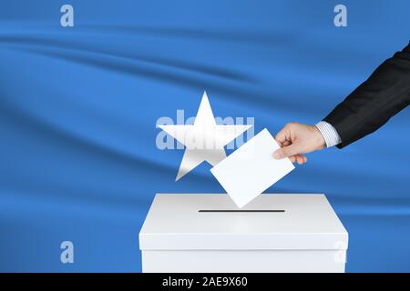 Wahlen in Somalia. Die Hand des Menschen, der seine Stimme in die Wahlurne setzt. Winkte Somalia Flagge auf Hintergrund. Stockfoto