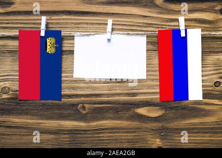 Hängenden Flaggen von und zu Liechtenstein und Russland zu Seil mit wäscheklammer mit Kopie Raum befestigt auf weißem Papier auf Holz- Hintergrund. Diplomatischen relat Stockfoto