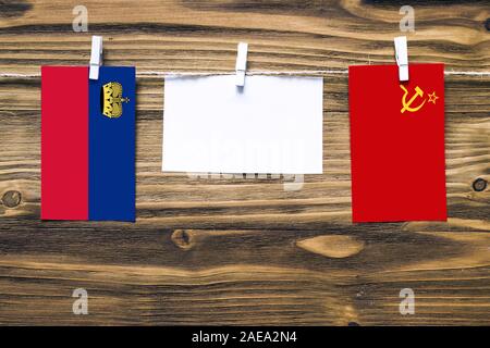 Hängenden Flaggen von und zu Liechtenstein und Sowjetunion Seil mit wäscheklammer mit Kopie Raum befestigt auf weißem Papier auf Holz- Hintergrund. Diplomatischen Stockfoto