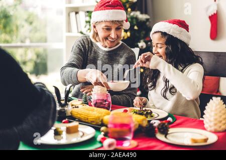 Glückliche Familie sind Abendessen mit lecker Essen und Wein Gläser mit Weihnachten Dekoration Weihnachten thematische Abendessen auf den Tisch zu Hause im Wohnzimmer r Stockfoto