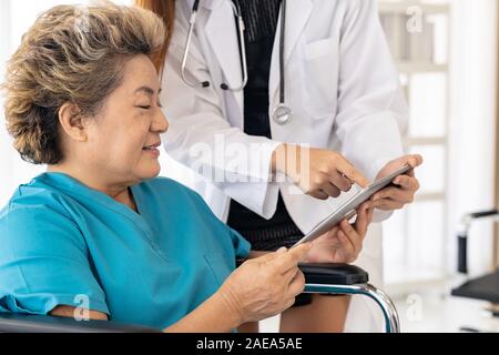Asiatische vertrauen Arzt mit digitalen tablet Ausdruck Gesundheit Interessen mit alten ältere Frau Patienten sitzen auf Rollstuhl Stockfoto