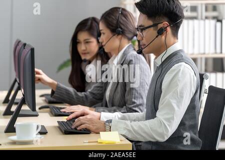Junger Erwachsener freundlich und Vertrauen Betreiber mann Agent mit Headsets, die in einem Call Center mit seinem Kollegen Team Service und der Stockfoto