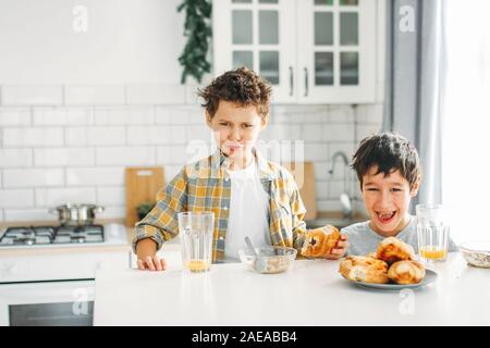 Zwei Geschwister tween Jungen echten Brüder mit lustigen Gesichter beim Frühstück auf helle Küche im Haus Stockfoto