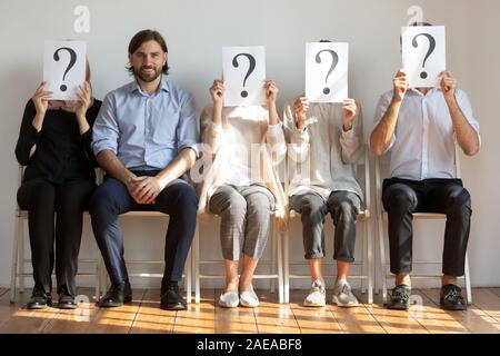 Selbstbewussten jungen Mann sitzt auf Stuhl in der Warteschlange von unbekannten Personen. Stockfoto