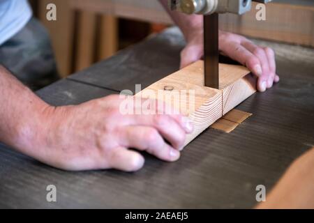 Tischler schneiden ein Stück Holz auf einer Bandsäge in Nahaufnahme auf seine Hände, als er Werke Stockfoto