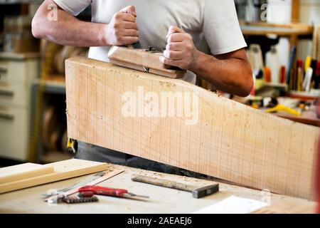 Tischler arbeiten mit einem Planer auf einen Holzblock Glättung der Oberfläche in der Nähe zu seiner Hände und Werkzeuge auf der Werkbank Stockfoto