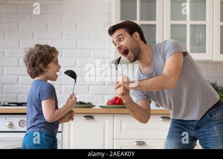 Vater tanzen mit Sohn holding Küche Löffel wie Mikrofon singen Stockfoto