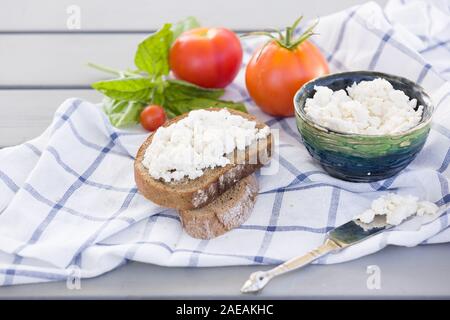 Der ökologische Landbau Hüttenkäse in einem grünen Schale, Scheibe Vollkornbrot mit hausgemachten Ricotta Käse serviert mit Tomaten und Basilikum auf Holzbrett Stockfoto