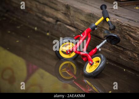 Die hellen Kinder Fahrrad stehend in einer Pfütze nach dem Regen. Das Kind das Fahrrad in einer großen Pfütze mit Graffiti wand Reflexion. Fun nach Regen. Outdoor ein Stockfoto