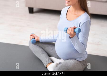 Nicht erkennbare schwangere Frau mit Kurzhanteln auf Yoga Matte Stockfoto