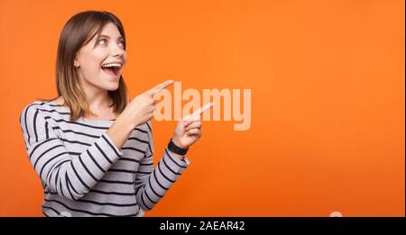Portrait von überrascht glückliche junge Frau mit braunen Haaren in gestreiften Shirt stehen, zu leeren Raum, der für Ansage, unglaubliche Nachrichten. indoor Stockfoto