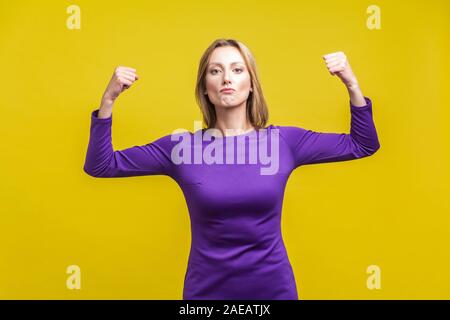 Weibliche Kraft und innere Stärke. Portrait von Stolz, erfolgreiche Geschäftsfrau in eleganter lila Kleid zeigen, Bizeps, Gefühl unabhängig und conf Stockfoto