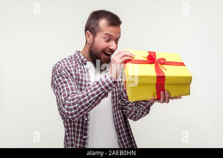 Portrait von aufgeregt, bärtigen Mann überrascht im casual Plaid Shirt auspacken Big vorzulegen, überrascht angenehm überrascht, was innen Geburtstag Stockfoto