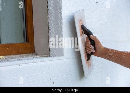 Hand eines Arbeitnehmers mit einem Werkzeug zum Schleifen und Glätten und sogar die Oberfläche einer Hauswand mit Styrofoam Dämmplatten isoliert. Stockfoto