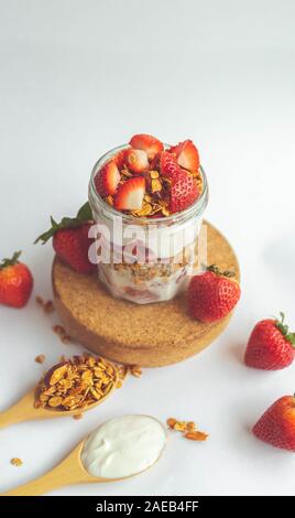 Ein Glas mit leckeren Parfaits aus gesundes Müsli, Erdbeeren und griechischer Joghurt auf weißem Hintergrund. Schuß im Winkel. Stockfoto