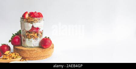 Ein Glas mit leckeren Parfaits aus gesundes Müsli, Erdbeeren und griechischer Joghurt auf weißem Hintergrund. Idee für Banner, Schuß im Winkel. Stockfoto