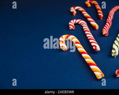 Weihnachts-Zuckerrohr. Auf klassisch blauem Hintergrund. Flach liegend. Weihnachtskomposition. Ein Fan von karamellgestreiften Zuckerrohrbonbons auf dunkelblauem Hintergrund Stockfoto