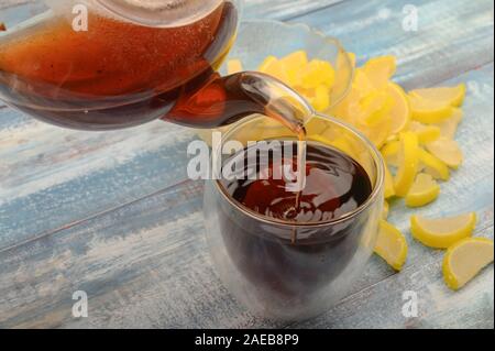 Schwarzer Tee ist aus einer Teekanne in ein Glas gegossen, Marmelade Zitronenscheiben auf einer hölzernen Hintergrund. Nahaufnahme Stockfoto