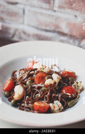 Roggen Pasta mit Kapern und Garnelen in weißem Porzellan Teller, Nahaufnahme, getönten Bild Stockfoto