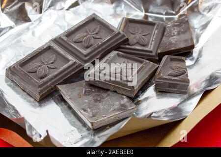 Zerbrochene Schokoriegel in offener Folienverpackung. Schokoladen-Tafel in einer Folie. Stockfoto