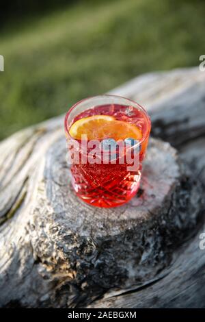 Cocktail Sommer in leuchtend roter Farbe mit Heidelbeeren und orange, stehend auf einem Holz- in einer Landschaft anmelden Stockfoto
