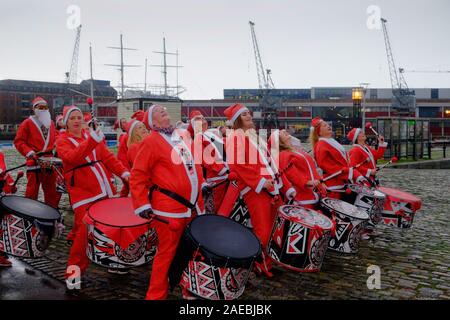 Harbourside, Bristol, UK, 8. Dezember 2019. Weihnachtsmänner laufen rund um den Hafen von Bristol für die Wohltätigkeitsorganisation Children's Hospice South West. Jeder Teilnehmer Geld für die Nächstenliebe, ob Sie Laufen, Joggen oder Laufen. Der Samba Band unterhalten die Beobachter. Die Nächstenliebe betreibt drei Hospize im Südwesten. Credit: Herr Standfast/Alamy leben Nachrichten Stockfoto