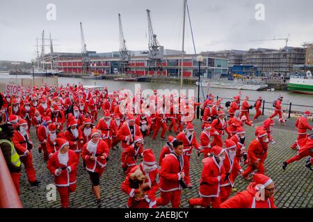 Harbourside, Bristol, UK, 8. Dezember 2019. Weihnachtsmänner laufen rund um den Hafen von Bristol für die Wohltätigkeitsorganisation Children's Hospice South West. Jeder Teilnehmer Geld für die Nächstenliebe, ob Sie Laufen, Joggen oder Gehen, die weniger aktiv helfen, indem Sie die Ausgaben im festlichen Dorf auf saisonale Gerichte. Die Nächstenliebe betreibt drei Hospize im Südwesten. Credit: Herr Standfast/Alamy leben Nachrichten Stockfoto