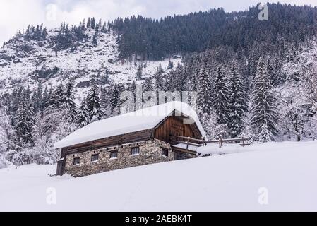 Stabile, Kuhstall für Kühe und Pferde. Bauernhof Gebäude aus Stein und Holz. Winter Berge in den Alpen. Das Gebäude, Bäume und Berge. Stockfoto