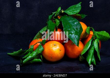 Orange Mandarinen Obst und grüne Blätter auf schwarzem Holz Schneidebrett und schwarzen Hintergrund Stockfoto