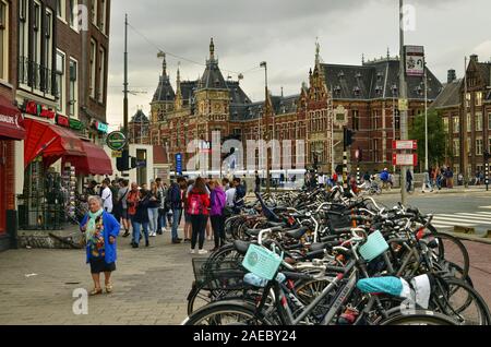 Amsterdam, Holland, August 2019. Seitliche Sicht auf drei Viertel der großen Hauptbahnhof. Von der Straße aus eine Reihe von geparkten Fahrräder führt das Auge Stockfoto