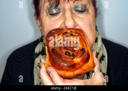 Frau essen ein Chelsea Brötchen Kuchen Stockfoto
