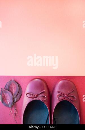 Stilvolle weibliche flache Schuhe in dunkelrote Farbe und Herbstlaub auf orange Farbe Papier Hintergrund mit Copyspace. Herbst Fashion Kollektion Konzept. Stockfoto