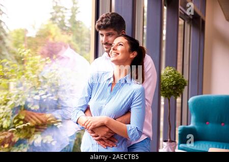 Portraitfotos der glückliche junge Paar stand am Fenster und genießt jeder des anderen Firma. Junge Frau, schauen aus dem Fenster, während schöner Mann st Stockfoto