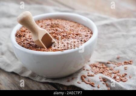 Weiße Schüssel ganzer Leinsamen, Leinsamen auf hölzernen Tisch. Stockfoto