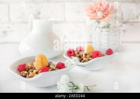 Bio Müsli mit Himbeeren für Frühstück in einem weißen Porzellan Tasse mit kleinen weißen Blüten auf einem hellen Hintergrund. Stockfoto