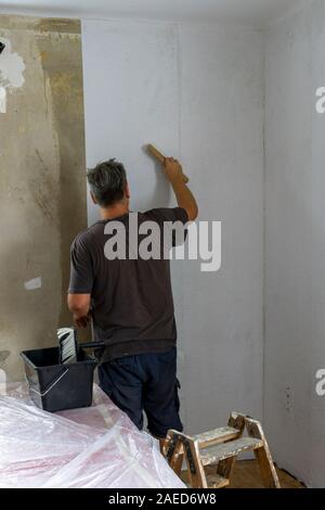 Kleben von Tapeten zu Hause. Männer sind das Aufstellen von Tapeten an der Wand. Stockfoto