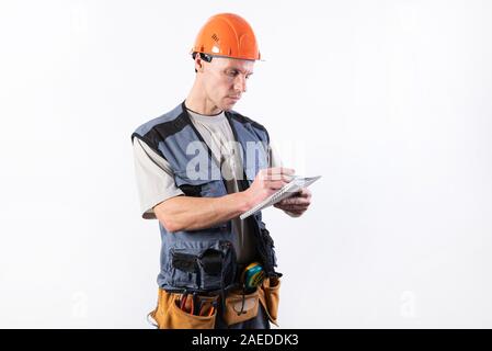 Builder mit einem Notizblock. In einen Helm und einen Bademantel. Schreibt Daten. Stockfoto
