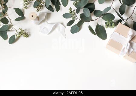 Kreative Zusammensetzung aus grünem berry Eukalyptus populues Blätter und Zweige, Geschenkbox und hölzernen Schieber mit Seidenband isoliert auf weißem Stockfoto