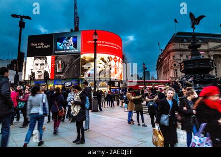 Menschen um am Piccadilly Circus am Abend Zeit hetzen mit dem kultigen Werbung in den Hintergrund, London, UK Stockfoto