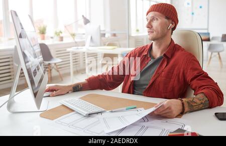 Portrait des modernen tätowiert Geschäftsmann mit Computer und Schreibtisch in geräumigen weiß die Arbeit im Büro Stockfoto