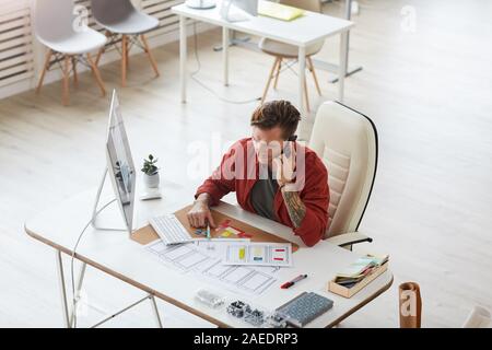 Hohen winkel Porträt des zeitgenössischen tätowiert Geschäftsmann sprechen per Telefon während der Arbeit am Schreibtisch in geräumigen Büro, Kopie Raum Stockfoto