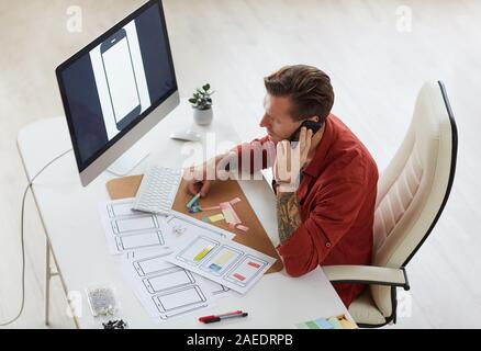 Hohe Betrachtungswinkel bei zeitgenössischen tätowiert Geschäftsmann sprechen per Telefon während der Arbeit am Schreibtisch in geräumigen Büro, Kopie Raum Stockfoto