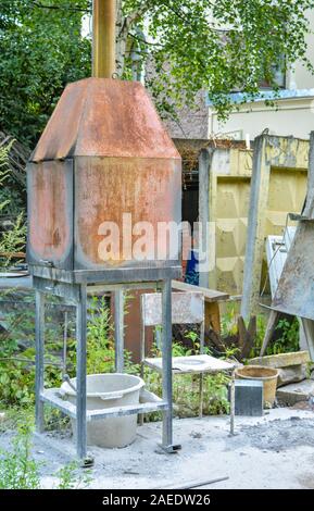Kleines rostiges Metall Verbrennungsanlage Herd im Sommer im Freien. Alten Ofen und Stuhl mit weißer Staub oder Asche auf Outdoor im Sommer Handwerk workshop Stockfoto