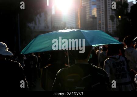 Ein demonstrant gesehen werden kann, die eine hellblaue Regenschirm, beleuchtet durch das Sonnenlicht. Diese Rallye markiert die sechs Monat Jahrestag der Proteste in Hongkong. Stockfoto