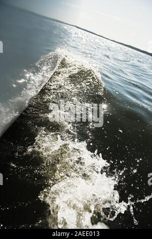 Spiegelbild im Wasser. Die Konturen eines weißen und blauen Boot im Wasser wider. Wellen und kleine Wellen auf der Oberfläche von einem See oder Teich. Sonnig Stockfoto