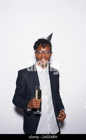 Taille bis Portrait von trendigen Afrikaner - Mann, Champagner Glas, während gegen den weißen Hintergrund bei Party posiert, geschossen mit Flash Stockfoto