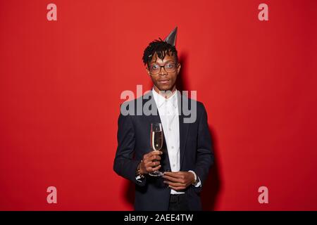 Taille bis Portrait von trendigen Afrikaner - Mann, Champagner Glas, während gegen den roten Hintergrund bei Party posiert, geschossen mit Flash Stockfoto