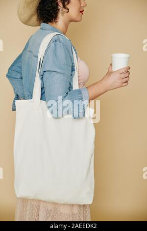 Zugeschnittenes Bild von stilvollen junge Frau mit Bettwäsche, wiederverwendbare Tasche trinken Papier Glas frisches Wasser Stockfoto