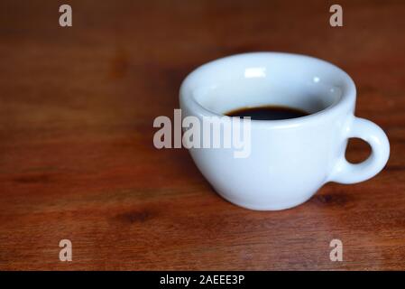 Eine weiße Alte Schale für Espresso steht mit Kaffee auf einem Holztisch Stockfoto