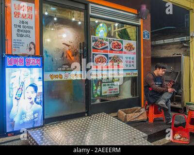 Restaurant Arbeitnehmer, der einen Bruch, der Mensch auf der Suche nach Smart Phone, rauchen eine Zigarette, draußen zu sitzen, night street, Gyeongbokgung, Seoul, Südkorea Stockfoto